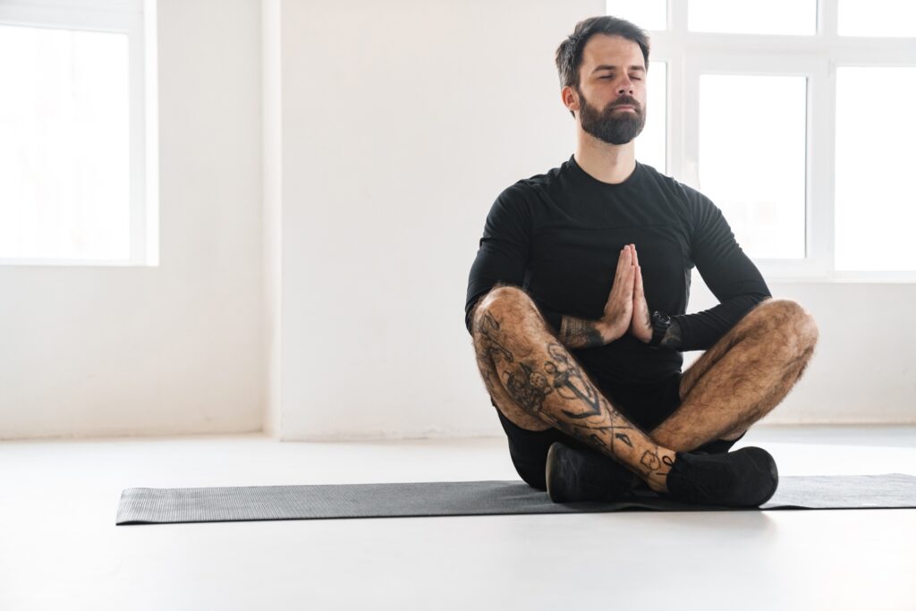 Bearded sportsman with tattoo meditating during yoga practice